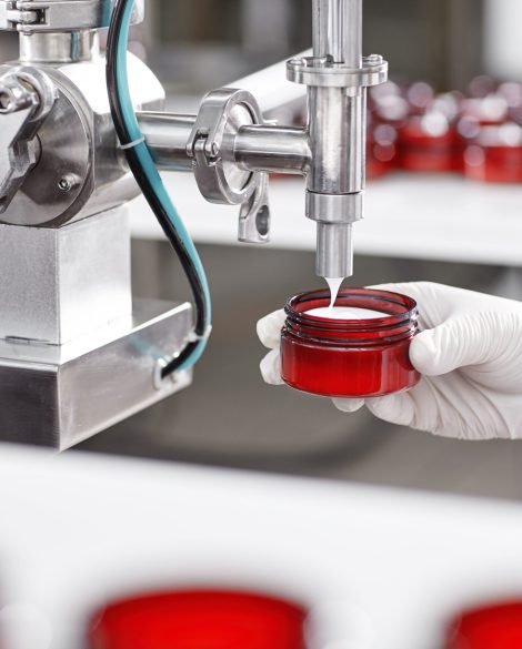 Portrait of big factory process of creating lotion for skincare. Researcher holding container under big metal tube pouring beauty cream isolated over working process at factory and many containers